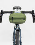 Green waterproof bar bag attached with magnetic fastenings to handlebars, studio setting.